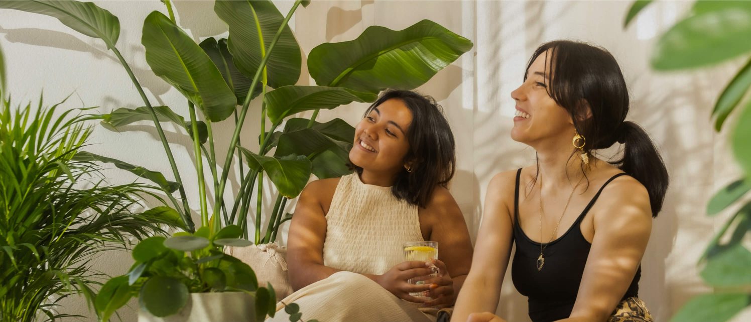 Two people sitting among houseplants, smiling and enjoying a relaxed conversation.